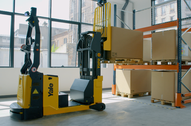 Chariot &agrave; m&acirc;t r&eacute;tractable robotis&eacute; en train de placer un carton sur le rayonnage d'un entrep&ocirc;t