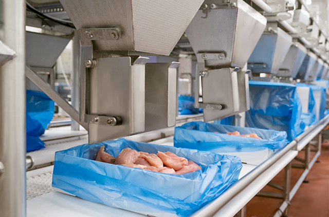 Machines processing containers of meat in blue plastic bags